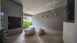 Um interior moderno com paredes, teto e chão de concreto. Há dois taboretes grandes, redondos e de cor clara.