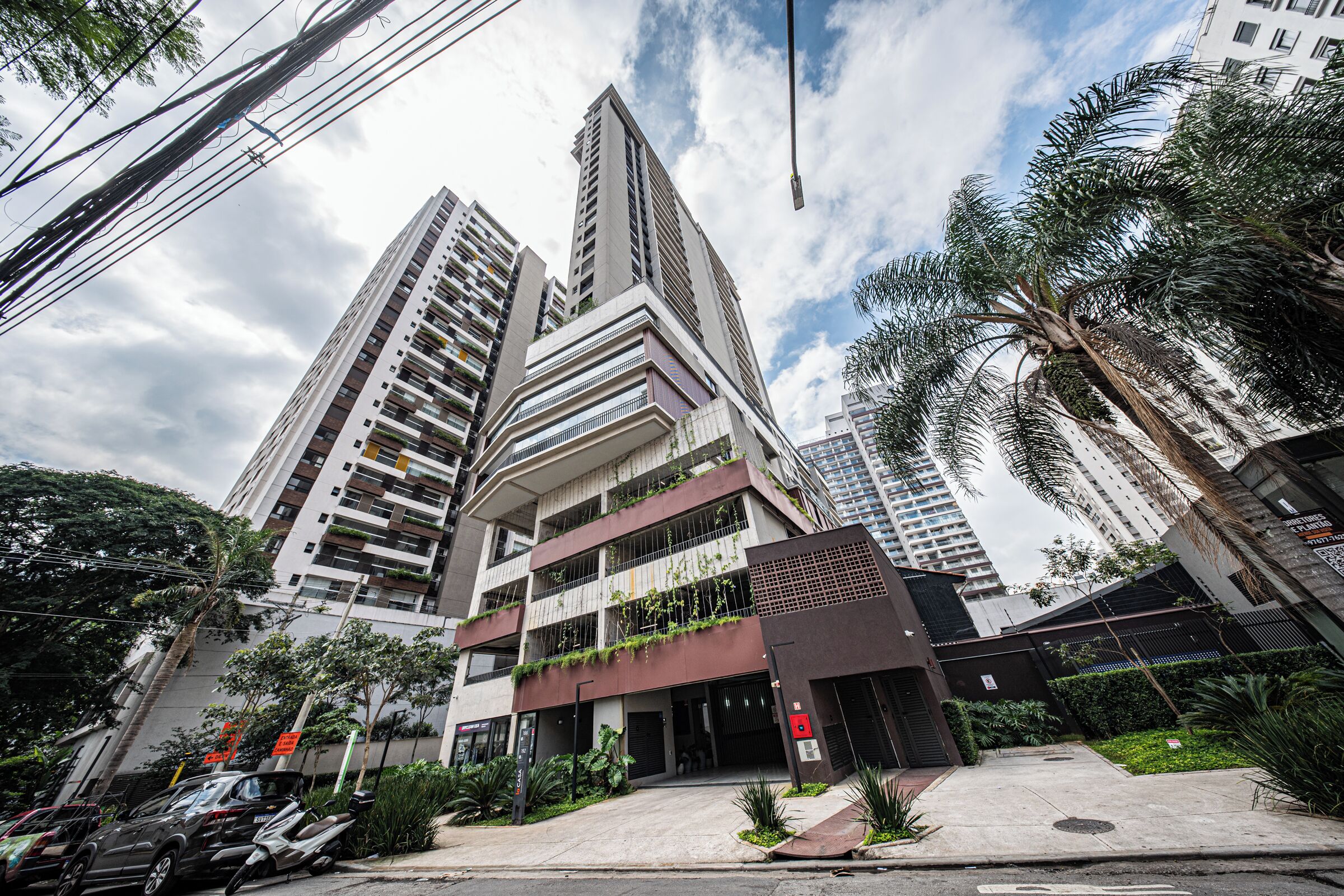 A multi-story building with balconies, a parking area, and surrounding greenery.