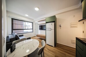 A compact living space with a dining area, a kitchenette, a built-in bench, and a window with blinds. - LA CASA PÁSSAROS (São Paulo)