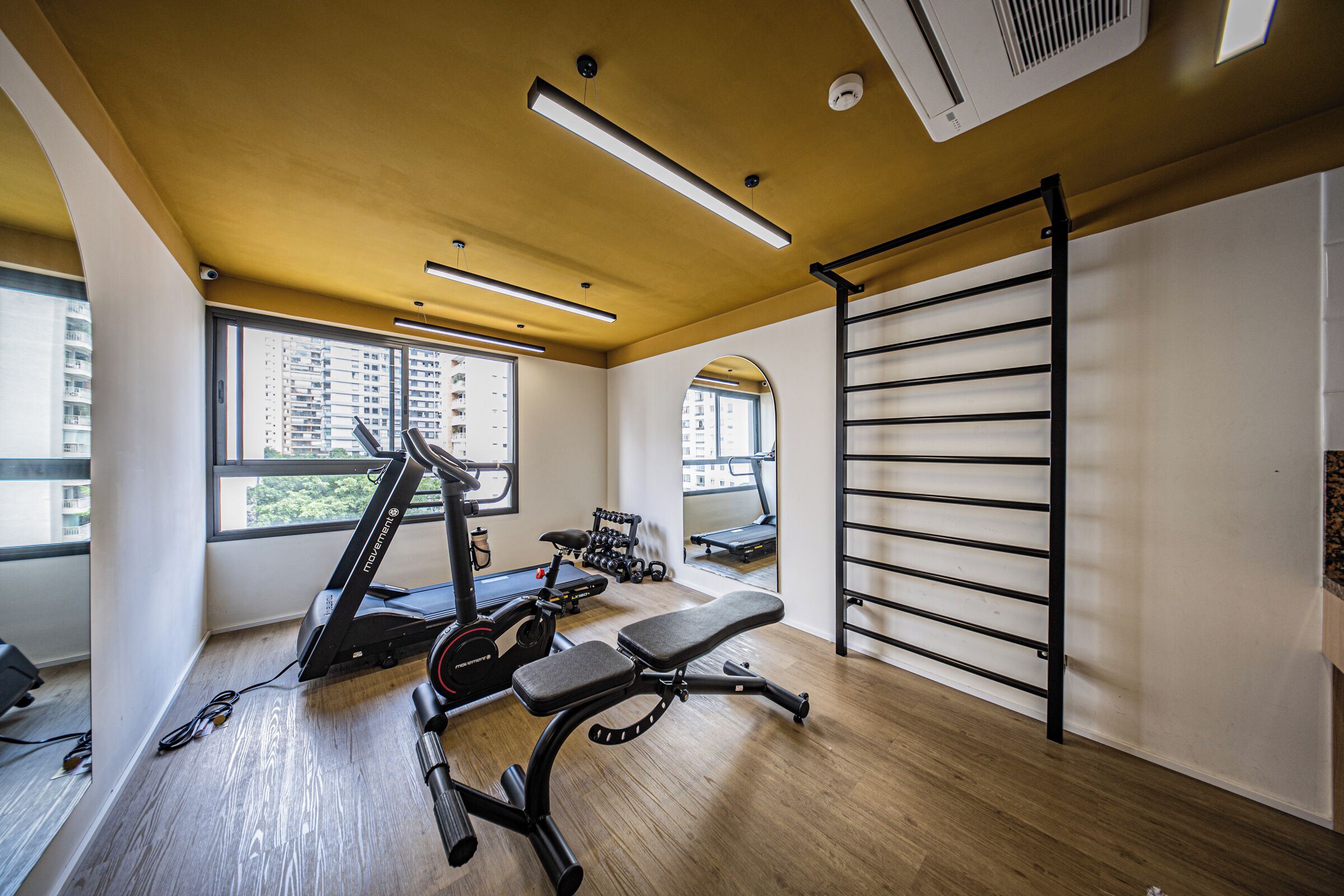 Une salle de sport équipée de matériel d’exercice, d’un tapis de course et d’un porte-haltères fixé au mur.