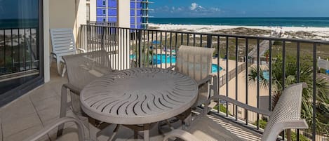 A balcony with a round table and chairs, a view of the beach, and a pool.