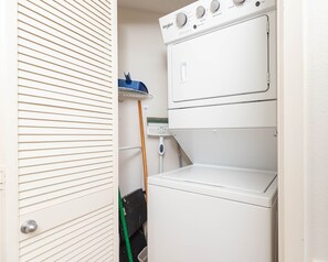A compact laundry room with a front-loading washer and dryer, a mop, and a broom. - Phoenix Viii 8302 2 Bedroom Condo (Orange Beach)