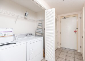 A laundry area with a washer and dryer, a hanging rack, and a door with a sign. - Phoenix Viii 81505 1 Bedroom Condo (Orange Beach)