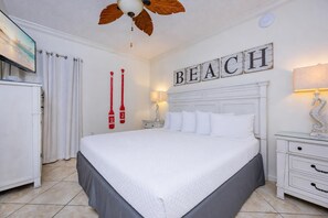 Ein Hotelzimmer mit einem großen Bett, einem Deckenventilator, einem Fernseher, einem Nachttisch und einem Wandzeichen mit der Aufschrift 'BEACH'.