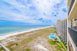 Blick auf einen Strand mit einem Hotel, einem Schwimmbad und blauem Himmel.