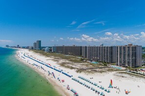 Un hotel frente a la playa con varios edificios altos, una playa de arena y un cielo azul despejado.