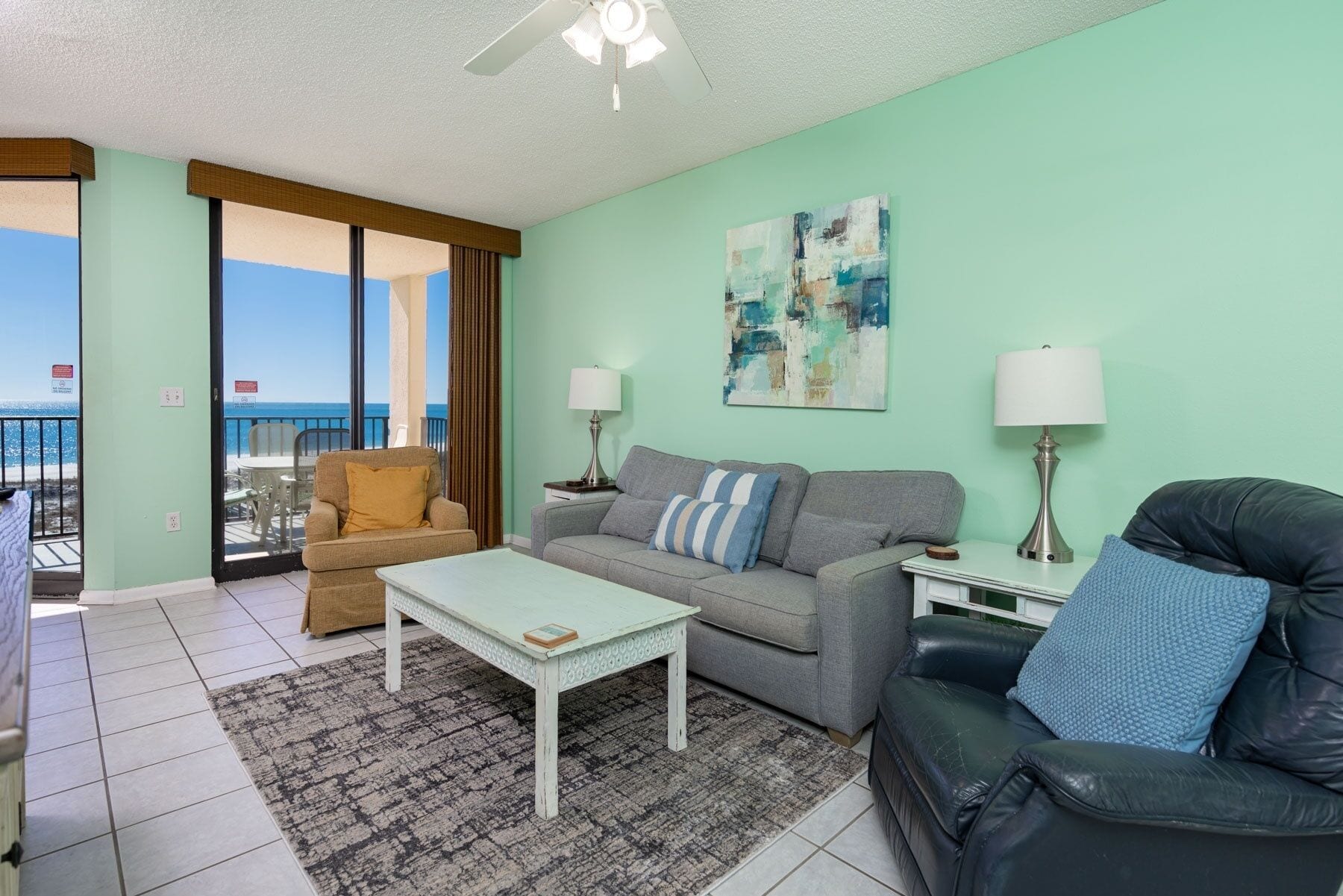 A living room with a sofa, armchair, coffee table, and a view of the ocean through a sliding door.