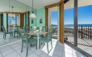 Un coin repas avec une table et des chaises, un luminaire suspendu et une vue sur la plage grâce à de grandes fenêtres.
