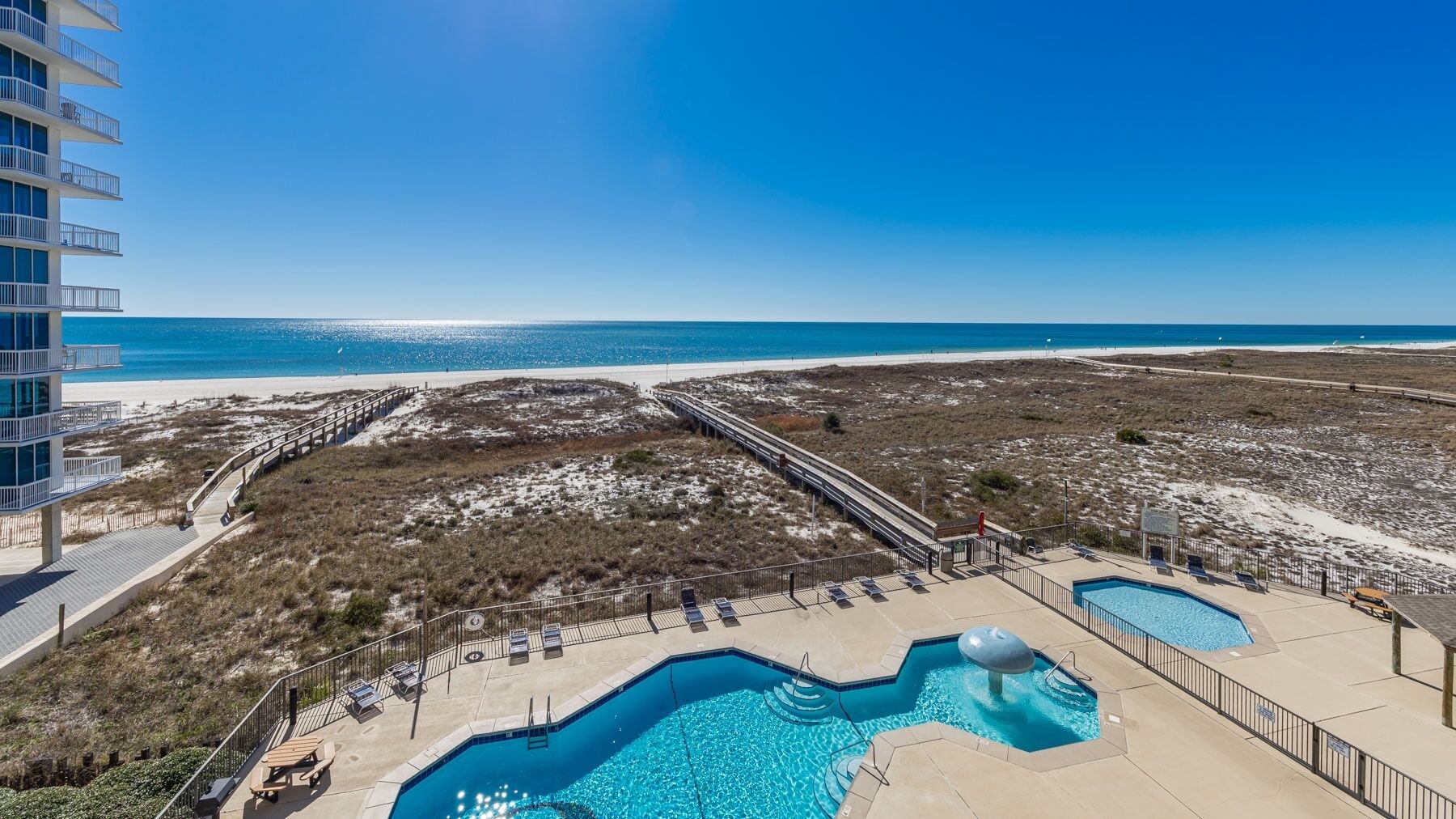 A resort with a pool area, a beach view, and a boardwalk leading to the beach.