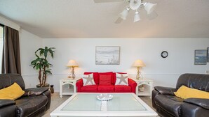 A living room with a red sofa, two black leather sofas, a white coffee table, and a ceiling fan. - Phoenix Vii 7712 3 Bedroom Condo (Orange Beach)