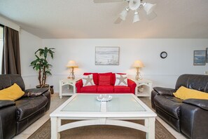 Ein Wohnzimmer mit einem roten Sofa, zwei schwarzen Ledersofas, einem weißen Couchtisch und einem Deckenventilator.