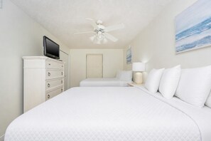 Ein Hotelzimmer mit einem Bett, einem Schminktisch, einem Fernseher, einem Deckenventilator und einem Bild an der Wand.