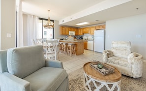 A living room with a sofa, a chair, a coffee table, and a dining area with chairs and a table. - Phoenix Viii 8301 3 Bedroom Condo (Orange Beach)