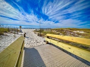 Ein hölzerner Steg führt zu einem Strand unter blauem Himmel.