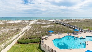 A beachside hotel with a swimming pool, lounge chairs, and a boardwalk leading to the beach. - Phoenix Viii 8306 3 Bedroom Condo (Orange Beach)