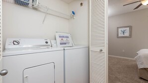 A laundry room with a washing machine, dryer, and a white door with a handle. - Phoenix Viii 8306 3 Bedroom Condo (Orange Beach)