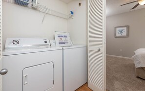 A laundry room with a washing machine, dryer, and a white door with a handle. - Phoenix Viii 8306 3 Bedroom Condo (Orange Beach)