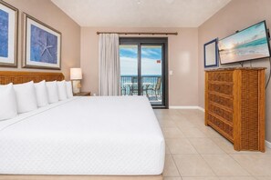 A hotel room with a large bed, a television, a balcony with a view of the ocean, and a wicker cabinet. - Phoenix Vii 71508 3 Bedroom Condo (Orange Beach)