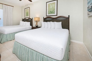 A hotel room with two queen beds, a nightstand with a lamp, and artwork on the walls. - Phoenix Vii 71508 3 Bedroom Condo (Orange Beach)