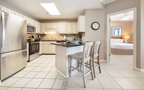 A kitchen with a refrigerator, oven, microwave, and a dining area with chairs. - Phoenix Vii 71508 3 Bedroom Condo (Orange Beach)