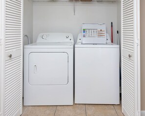 A compact laundry room with a front-loading washer and dryer, a control panel, and a red pen on the dryer. - Phoenix Vii 7708 3 Bedroom Condo (Orange Beach)