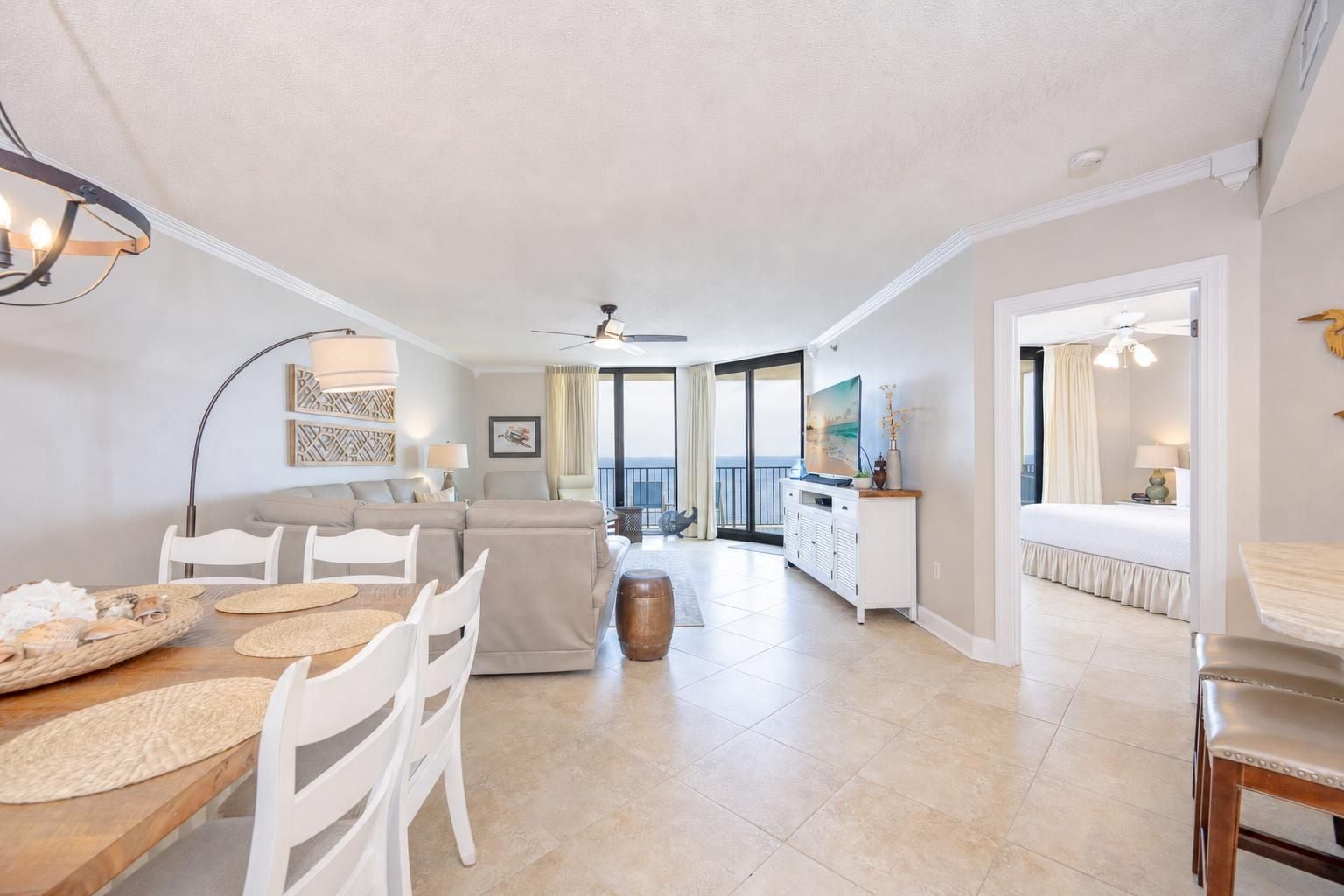 A spacious living area with a dining table, chairs, a sofa, and a balcony with a view.