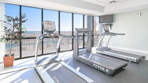 Ein Fitnessraum mit Laufbändern, einem Ergometer und einem Rudergerät, mit großen Fenstern und Blick ins Freie.