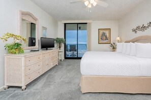 Quarto de hotel com uma cama grande, televisão em uma cômoda, varanda com vista e ventilador de teto.