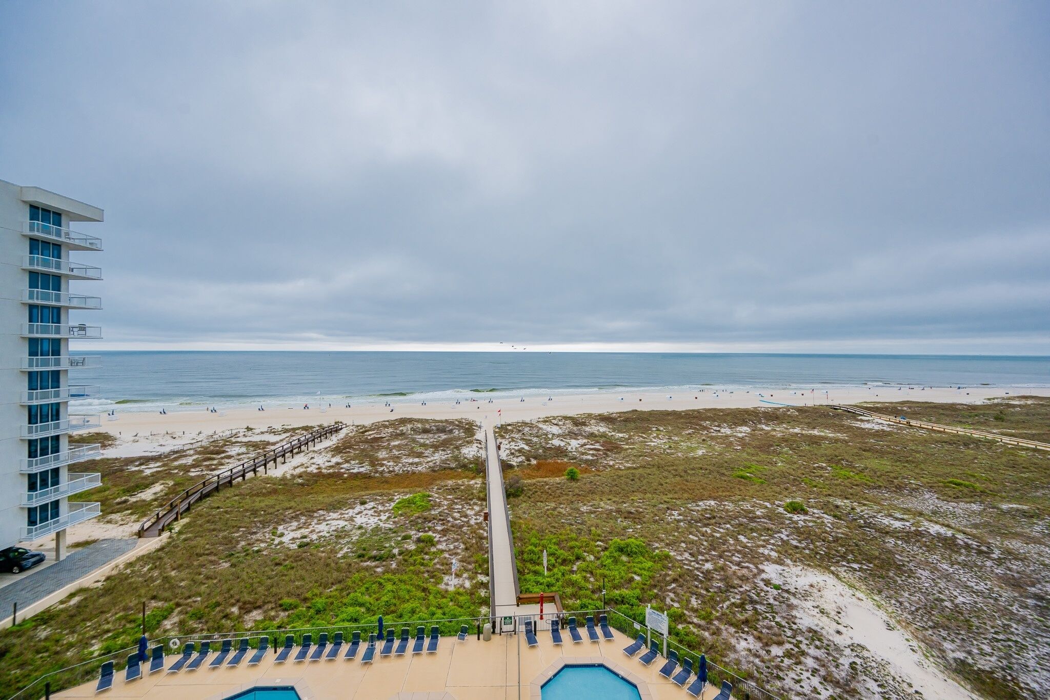 A beach view from a resort with a pool area, a boardwalk, and a building with balconies.
