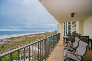 Ein Balkon mit Blick auf Strand und Meer, Sitzgelegenheiten im Freien und ein Gebäude im Hintergrund.