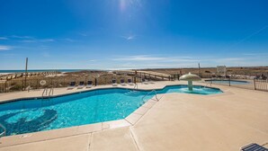 A swimming pool with a view of the beach and a wooden deck with lounge chairs. - Phoenix Viii 8706 3 Bedroom Condo (Orange Beach)