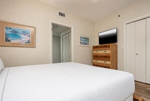 Un dormitorio con una cama, un televisor, un aparador de madera y dos cuadros en la pared.