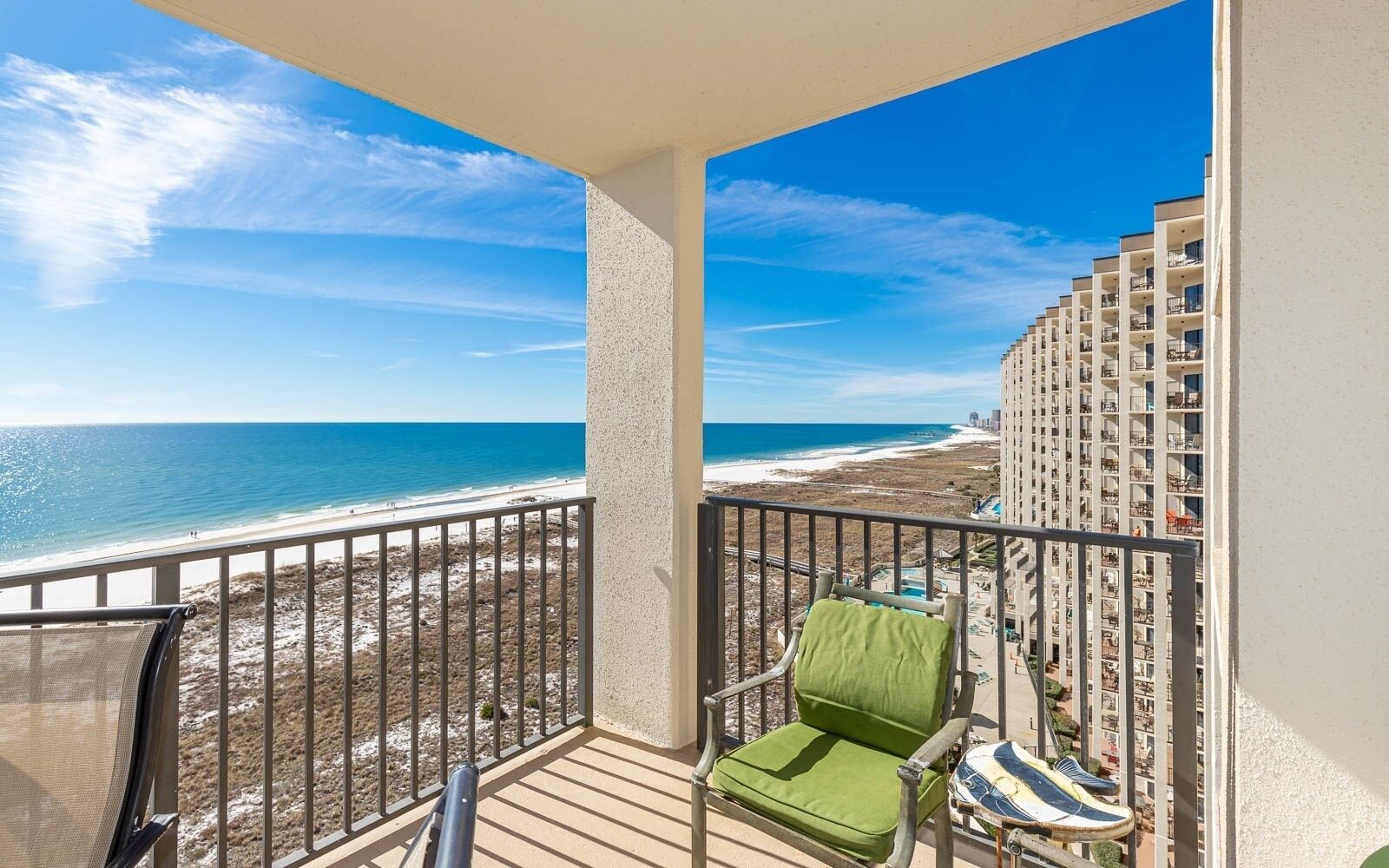 Ein Balkon mit Blick auf Strand und Meer, ein Stuhl und ein kleiner Tisch mit einem Handtuch.