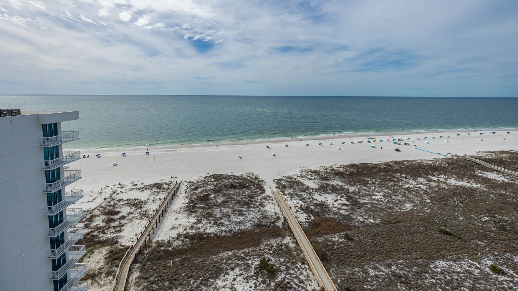 A beach with a boardwalk, a building with balconies, and a clear view of the ocean.