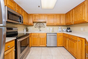 A kitchen with wooden cabinets, stainless steel appliances, a dishwasher, and a microwave. - Phoenix Vii 7808 3 Bedroom Condo (Orange Beach)