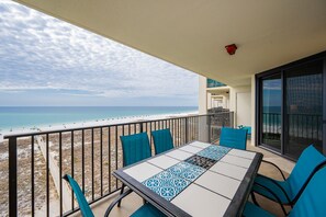 Ein Balkon mit Tisch und Stühlen, der Blick auf einen Strand mit blauem Himmel bietet.