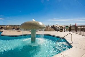 A swimming pool with a central fountain, surrounded by a tiled deck and a metal fence. - Phoenix Viii 8102 2 Bedroom Condo (Orange Beach)