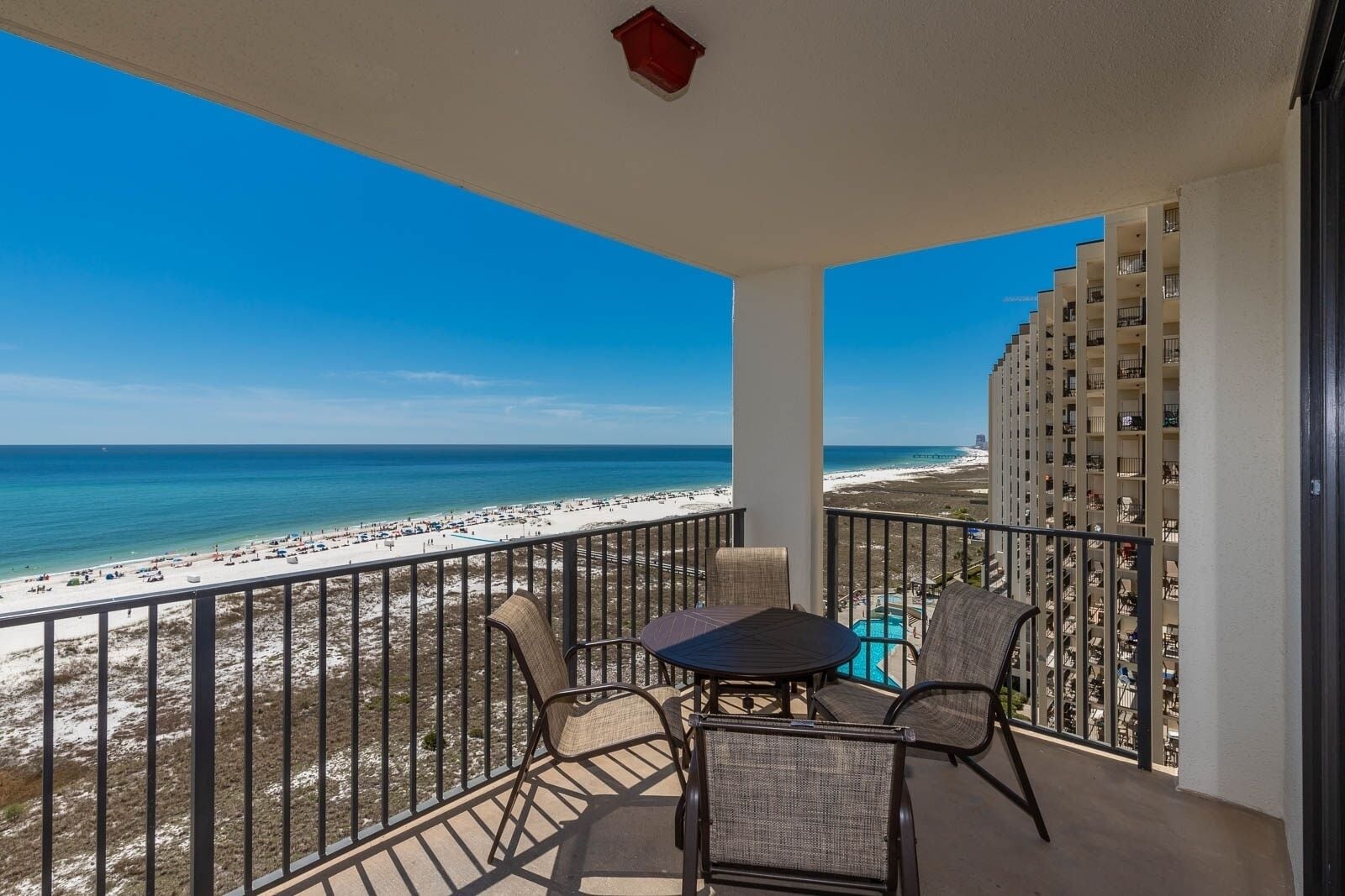 A balcony with a view of the beach, a pool, and a high-rise building.