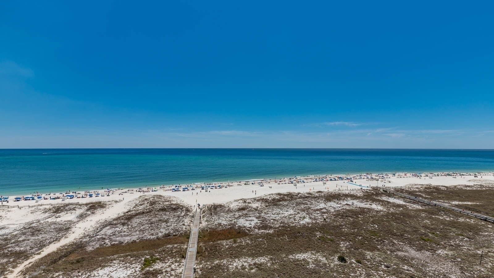 A beach with a wooden boardwalk leading to the shore, sandy beach, and clear blue sky.