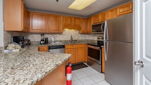 A kitchen with wooden cabinets, granite countertops, a stainless steel refrigerator, a microwave, an oven, and a dishwasher. - Phoenix Viii 81002 2 Bedroom Condo (Orange Beach)