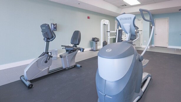 A gym with cardio machines, a weight bench, and a door in the background. - Phoenix Viii 81206 3 Bedroom Condo (Orange Beach)