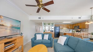 A living room with a TV, sofas, a coffee table, and a ceiling fan. - Phoenix Viii 81206 3 Bedroom Condo (Orange Beach)