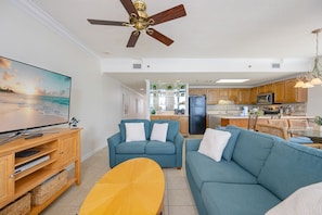 A living room with a TV, sofas, a coffee table, and a ceiling fan. - Phoenix Viii 81206 3 Bedroom Condo (Orange Beach)