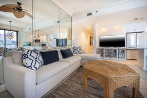 A modern living room with a sofa, a television, and a woven coffee table. - Phoenix Viii 8106 3 Bedroom Condo (Orange Beach)