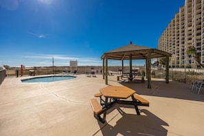 A pool area with a gazebo, picnic table, and lounge chairs. - Phoenix Viii 8106 3 Bedroom Condo (Orange Beach)