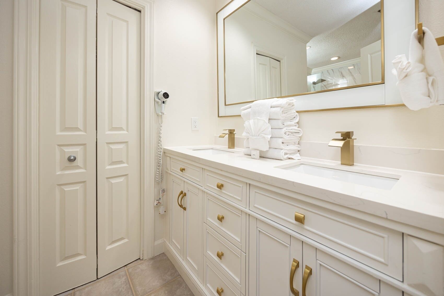A bathroom with a white vanity, gold handles, a large mirror, and a towel rack.