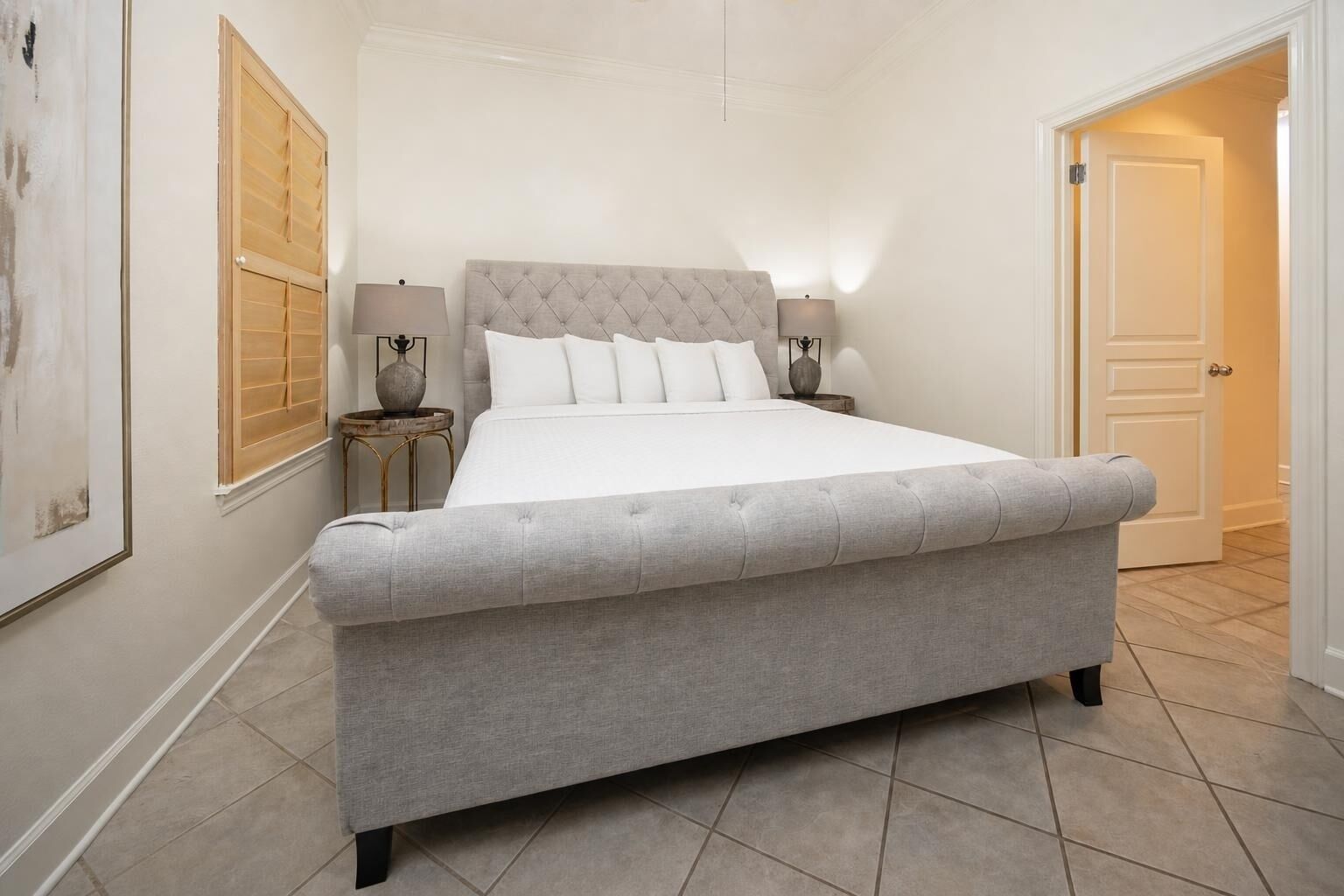A bedroom with a large bed, two bedside tables with lamps, a door, and a framed picture on the wall.