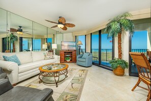 A spacious living room with a large sofa, a round coffee table, and a television. There is a balcony with a view of the ocean. - Phoenix Vii 7201 3 Bedroom Condo (Orange Beach)