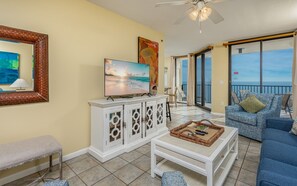 A living room with a TV, a sofa, a coffee table, and a balcony with a view. - Phoenix Viii 8905 1 Bedroom Condo (Orange Beach)