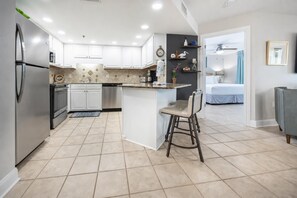 A modern kitchen with white cabinets, a stainless steel refrigerator, and a bar area with a stool. - Phoenix Vii 7912 3 Bedroom Condo (Orange Beach)